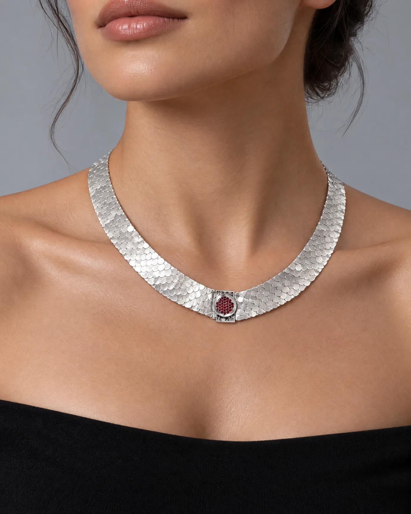 Flat fish-scale silver collar necklace with a round garnet pomegranate centre, worn with a black top