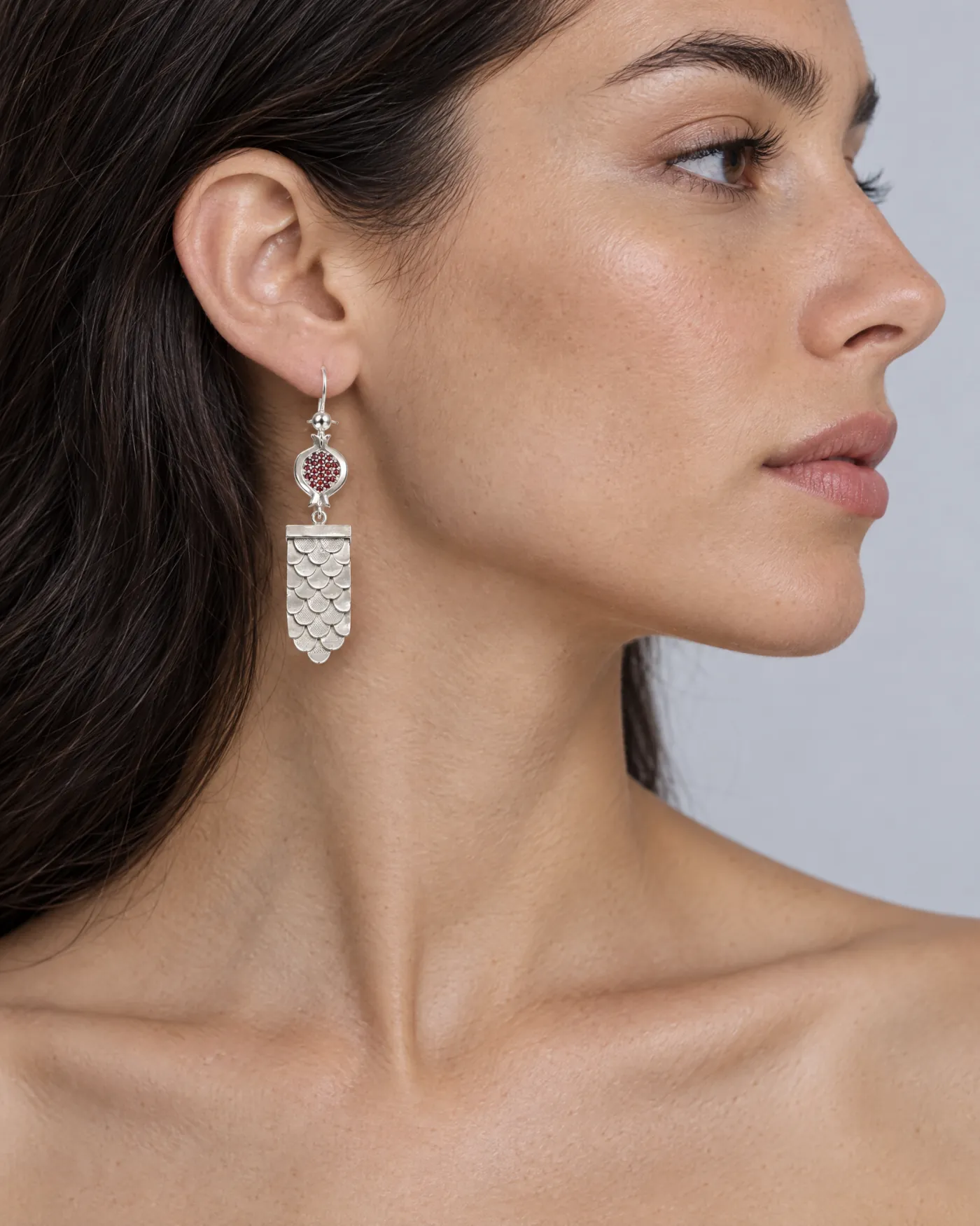 Silver drop earring with a garnet pomegranate and a fish-scale panel, seen in side profile