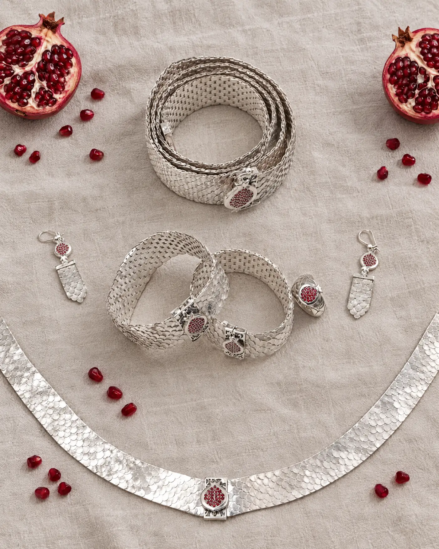 The full Fish Scale silver collection laid out on linen with halved pomegranates
