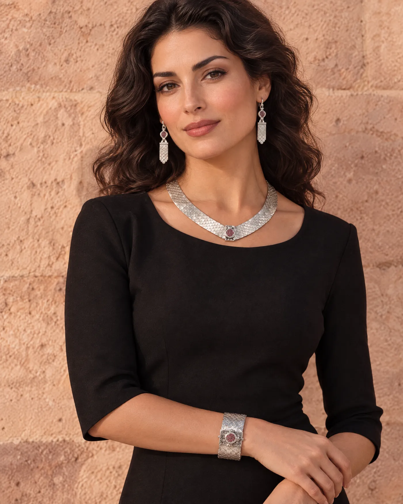 Woman in a black dress wearing the Fish Scale collar, earrings and cuff against a tuff stone wall