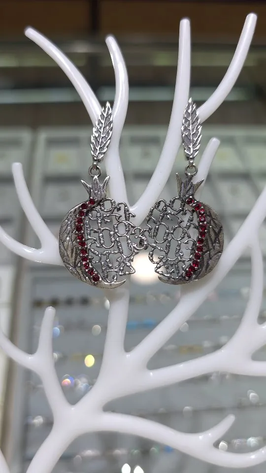 Silver pomegranate drop earrings with red stones on a white coral stand